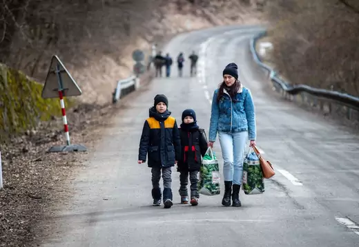 A woman with two children and carrying bags walk on a street to leave Ukraine after crossing the Slovak-Ukrainian border in Ubla, eastern Slovakia, close to the Ukrainian city of Welykyj Beresnyj, on February 25, 2022, following Russia's invasion of the Ukraine.