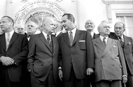 President Dwight D. Eisenhower, then-Senator Lyndon B. Johnson, and Secretary of State John Foster Dulles stand together with other guests at the White House. 