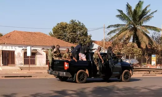 A group of soldiers are seen riding in a military truck on a deserted street.
