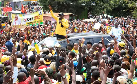 A crowd of people surrounds a car with William Ruto, a candidate for the Kenyan presidency, standing in the sun roof.