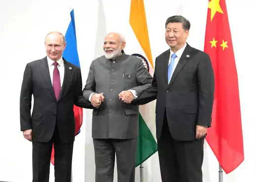 Leaders of Russia, India, and China hold hands while posing for a picture wearing formal attire with their respective flags in the background.
