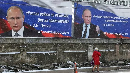 A woman walks past boards with portraits of Russian President Vladimir Putin in Simferopol, Crimea March 11, 2022. The boards read: "Russia doesn't start wars, Russia ends them" (L), "We want the demilitarisation and denazification of Ukraine".