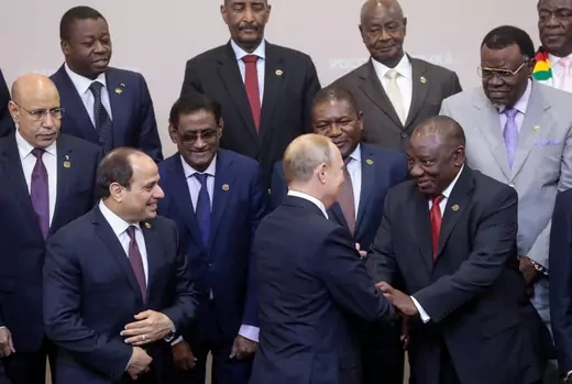 Vladimir Putin is shaking the South African president's hand while surrounded by other African leaders all wearing formal attire.