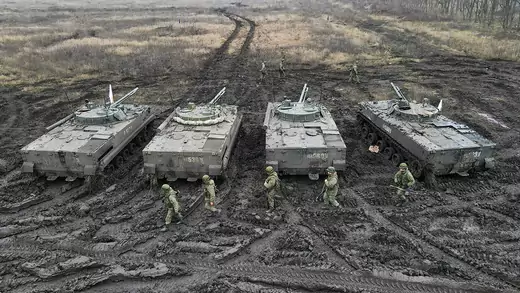 Russian service members walk past BMP-3 infantry fighting vehicles during tactical combat exercises