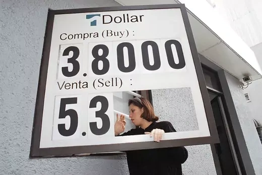 A woman changes a sign showing the U.S. dollar to Mexican Peso exchange rate.