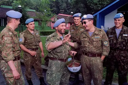 Six Ukrainian UN peacekeepers with blue berets laugh.