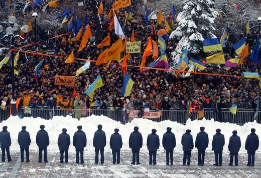 A line of police officers facing a crow of protesters with banners and Ukrainian flags.