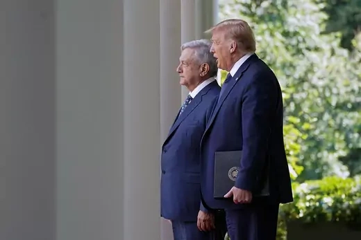 President Trump, holding a binder, and Mexican President Lopez Obrador stand outside, in front of columns, at the White House.