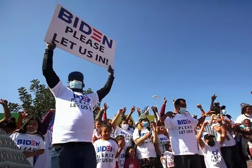 Protesters hold up signs saying "Biden, Please Let Us In".