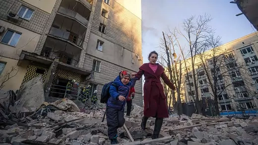 A woman with a child evacuates from a residential building damaged by shelling by Russian forces in Kyiv, Ukraine, in March 2022.