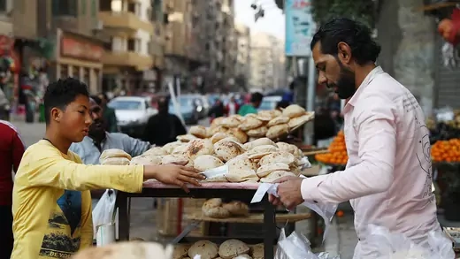 Un garçon remet de l'argent à un homme qui vend du pain sur un marché en plein air au Caire