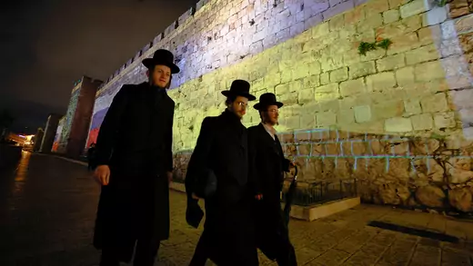 Three Orthodox Jewish men walk past a massive Ukrainian national flag that is projected on the walls of Jerusalem's Old City.