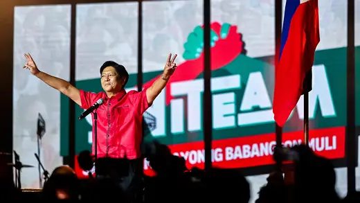 Ferdinand Marcos Jr. stands on a stage and makes peace signs with his hands.
