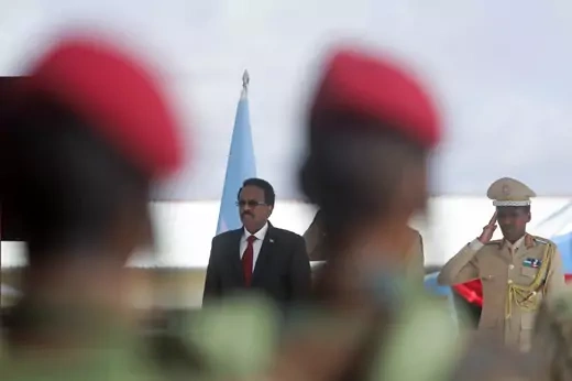 Somalia's president is seen in a picture taken with blurred soldiers in the foreground. A military officer to the president's left stands and salutes.