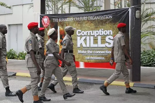 Military personnel walks in front of a sign that reads "corruption kills."