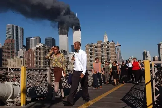 People walk over the Brooklyn Bridge as the world trade center burns.