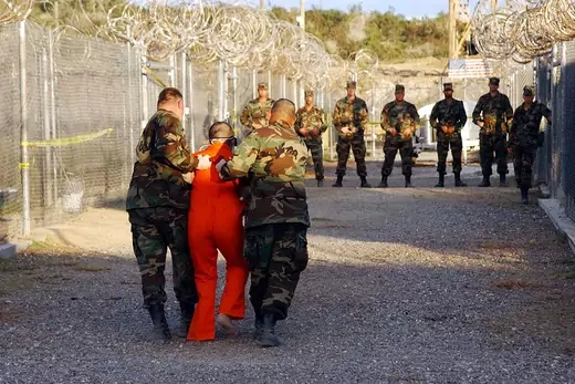 U.S. military police escort a detainee in orange jumpsuit to his cell in Camp X-Ray at Guantanamo Bay in January 2002. 