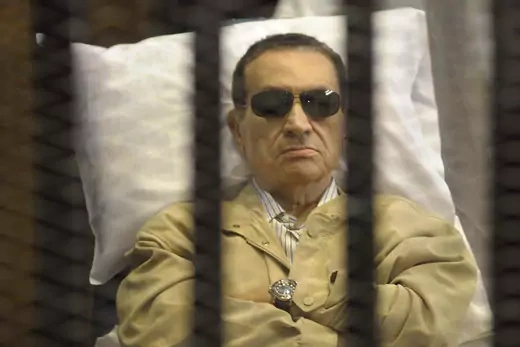 Hosni Mubarak wearing sun glasses and arms crossed, sits in a cage in a Cairo courtroom 