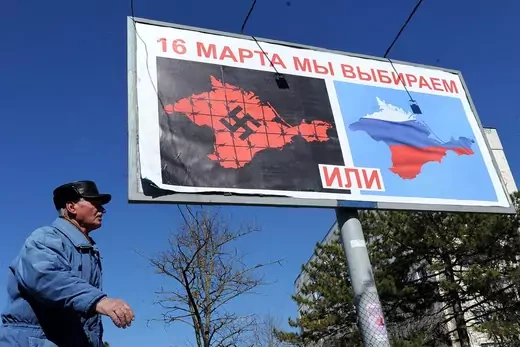 A man passes by a campaign poster in Crimea comparing Ukrainian control to Nazism and urges voters to choose to join Russia instead.