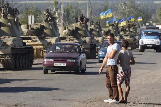 Two men watch a column of Ukrainian tanks as they roll through the streets.