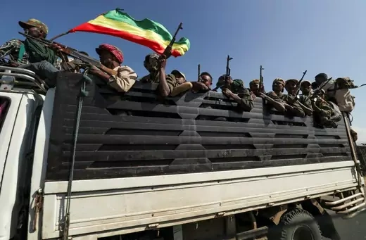 A group of Ethiopian militia members ride in the back of a truck, carrying an Ethiopian flag and brandishing assault rifles.