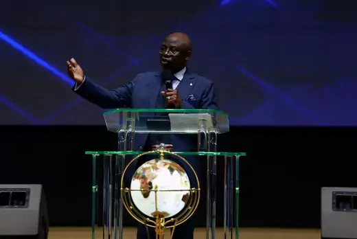 Pastor lectures with a microphone and gestures with his arm wearing a formal attire. 