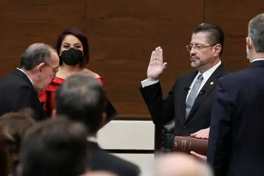 Rodrigo Chaves stands in the middle of a group of Costa Rican officials with his right hand raised and left hand on a Bible.