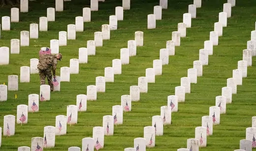 A soldier of the 3rd U.S. Infantry Regiment places flags on headstones in Arlington National Cemetery ahead of Memorial Day on May 26, 2022