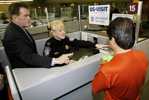 U.S. Homeland Security Secretary Tom Ridge assists a foreign airline passenger getting fingerprinted at an airport security checkpoint.