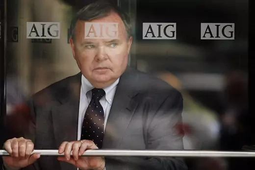 A male employee of AIG, looking worried, is seen through the window of an AIG office.
