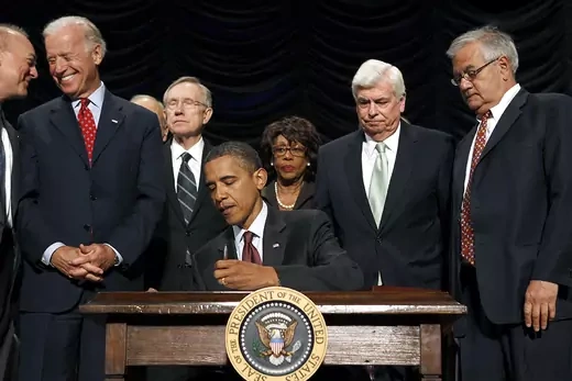 President Obama, surrounded by lawmakers and sitting at desk, signs the Dodd-Frank Wall Street Reform and Consumer Protection Act into law in Washington, DC.