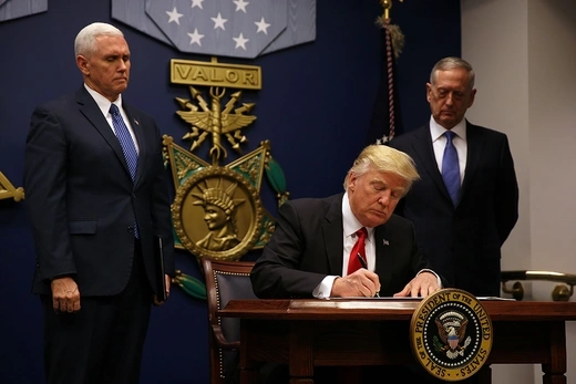 U.S. President Donald Trump is seen at desk signing an executive order, while Vice President Mike Pence and Secretary of Defense James Mattis look on.