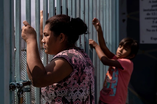 A Central American migrant  woman looks on from a fence at a shelter for migrant women and children in Tijuana, Mexico.