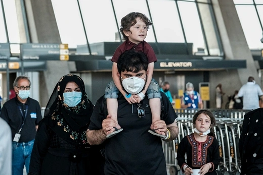 Photo showing an Afghan migrant father carrying his son on his shoulders accompanied by his wife and daughter, arriving at Dulles airport.  