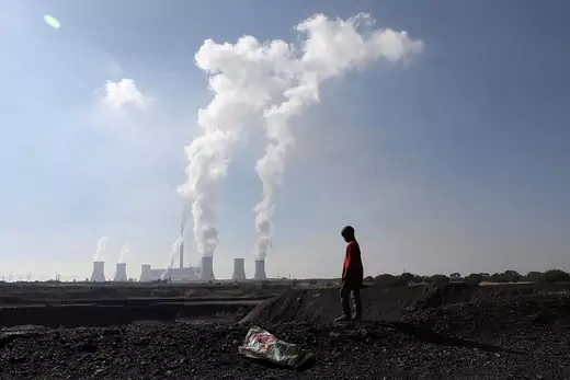 A boy stands in front of coal-fired power plants billowing smoke into the sky.