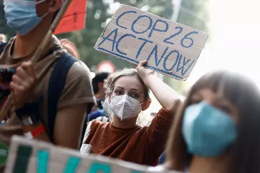 A young woman wearing a medical mask holds a sign reading "COP26 act now."