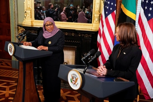 Tanzania's President Hassan wearing a head covering speaks at a podium with Vice President Harris to her left. 