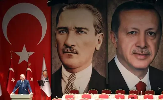 Recep Tayyip Erdogan speaking in front of massive Turkish flags and portraits of himself and Mustafa Kemal Ataturk 