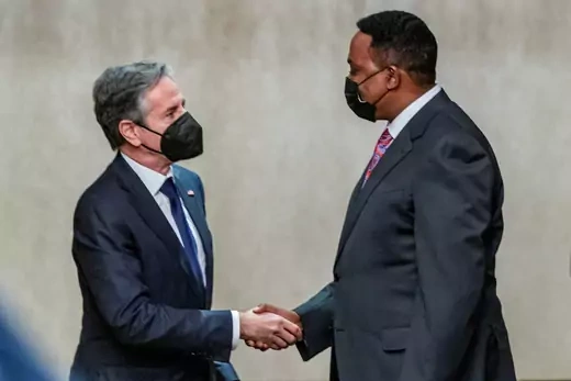 Secretary Anthony Blinken shakes hands with Workneh Gebeyehu from the Intergovernmental Authority on Development. Both wearing suits, ties, and black face masks. 