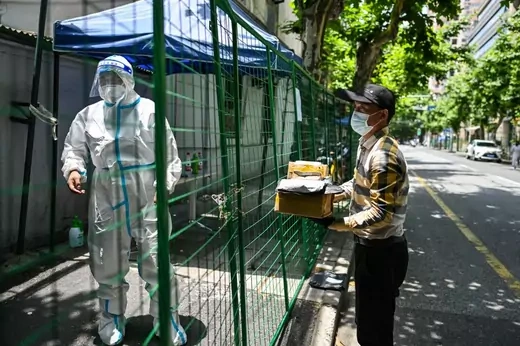 A delivery worker arrives with an order while a worker in protective gear looks on behind fencing under Covid-19 lockdown in the Xuhui district of Shanghai on June 8, 2022