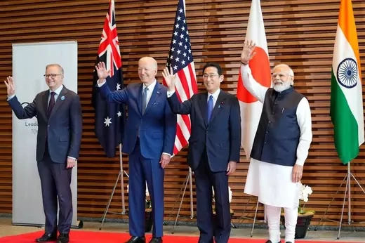 The four leaders of the quad stand in front of a wood background with the flags of all four countries behind them.