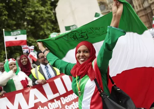 A woman wearing a hijab raises the Somaliland flag in the air while smiling