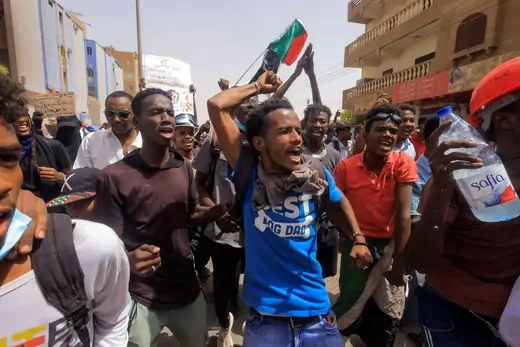 Several protesters march with their hands raised and flags waving down the streets of Sudan. 