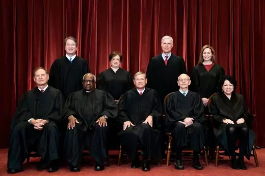 The nine Supreme Court Justices sit in front of a burgundy curtain in an official photo.