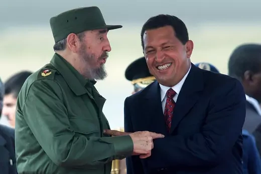 Fidel Castro and Venezuelan president Hugo Chávez point at each other, smiling.