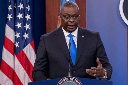 Lloyd Austin gestures in front of a podium with an American flag on the left in the photo.