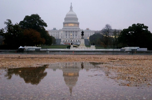 The U.S. Capitol building is seen reflected in a puddle at sunrise on November 6, 2018.