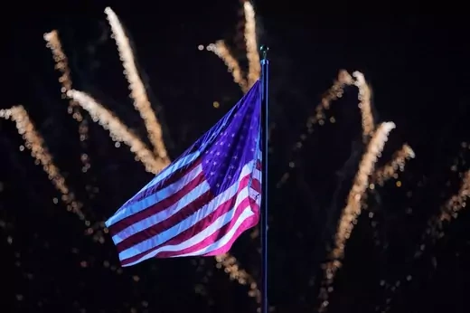 A U.S. flag waves in front of white fireworks. 
