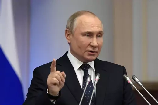 Vladimir Putin holds his finger up as he speaks in front of two microphones.