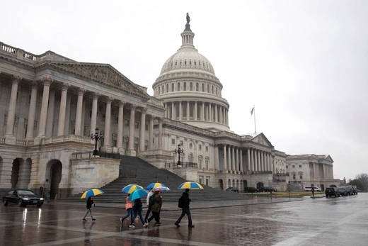 People carrying yellow and blue umbrellas walk in the rain outside the U.S. Capitol Building.